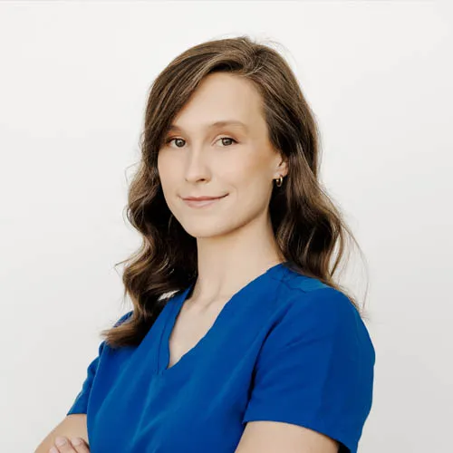 Meet the team: A portrait of a woman with long, light brown hair, wearing a blue blouse, smiling subtly at the camera against a white background. She has a gentle, confident demeanor.