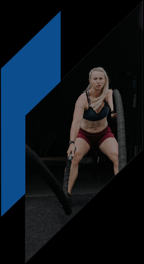 A woman in workout gear is intensely flipping a large tire in a gym, with a focused expression. The image has a blue geometric shape on the left side titled "What We Treat.